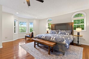 A bedroom with a large bed, a bench, two bedside tables, and a ceiling fan. - Calm Water Cove | Private Dock on Lake James, Game Room, Fire Pit & Spa Suite — Dogs Welcome! (Nebo)