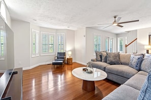 A spacious living room with hardwood floors, a ceiling fan, a sofa set, and a coffee table. - Calm Water Cove | Private Dock on Lake James, Game Room, Fire Pit & Spa Suite — Dogs Welcome! (Nebo)