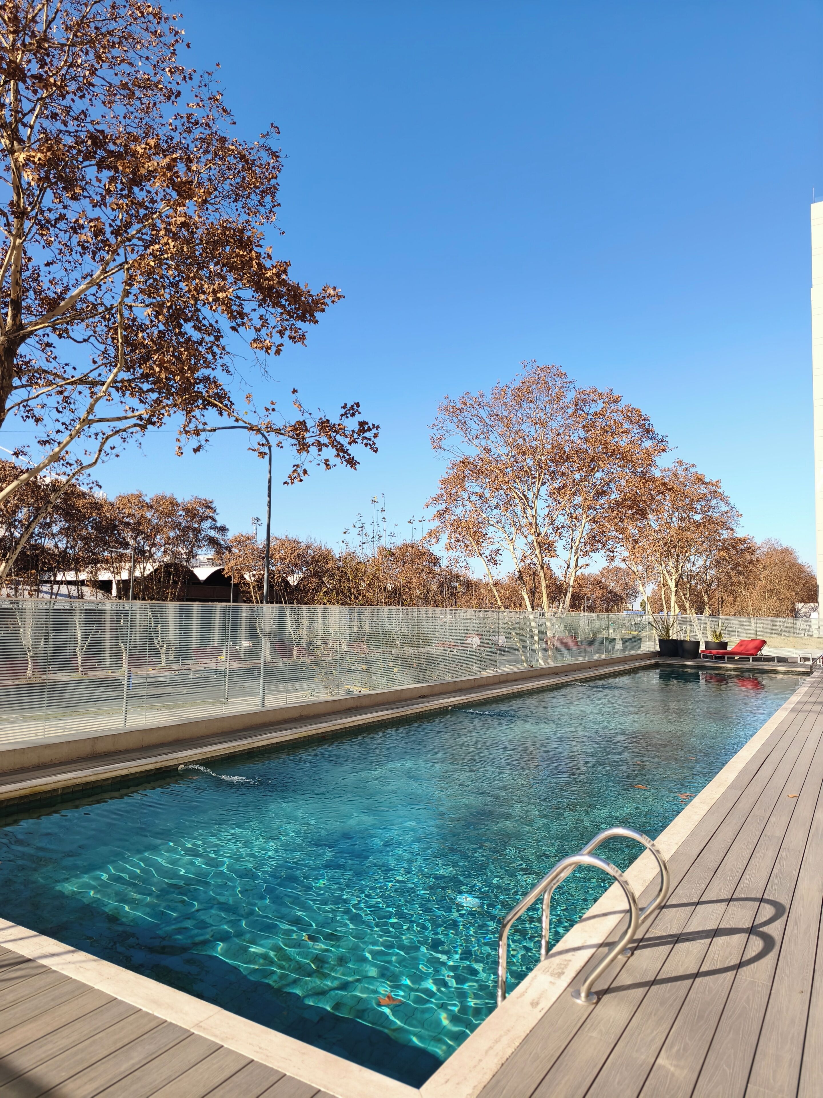 Una piscina cristalina con cubierta de madera, rodeada de árboles y una valla.