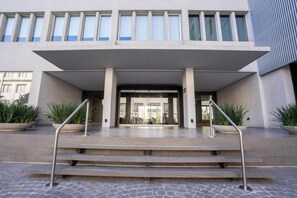 Een gebouwtoegang met een overdekte veranda, trappen en bloempotten.