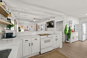 A modern kitchen with white cabinetry, a central island, and a built-in oven. - Tiki Time - 4BR Beach House w/ Hot Tub + Ocean Views | Sleeps 10 (North Myrtle Beach)