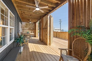A wooden deck with a ceiling fan, outdoor furniture, and a view of the ocean. - Tiki Time - 4BR Beach House w/ Hot Tub + Ocean Views | Sleeps 10 (North Myrtle Beach)