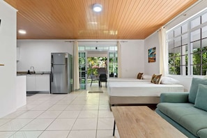A modern room with a bed, a sofa, a dining table, and a kitchen area.