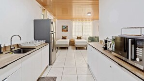 Cocina compacta con refrigerador, microondas y pileta. Hay dos camas con almohadones y un sofá verde.
