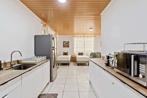 A compact kitchen with a refrigerator, microwave, and sink. There are two beds with pillows and a green sofa.