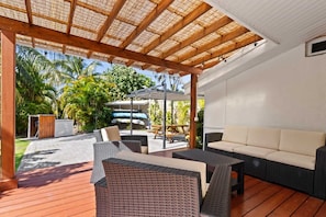Une terrasse extérieure aménagée avec des meubles en osier, une plateforme en bois et un espace couvert doté d’un toit de chaume.