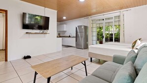 Una sala de estar moderna con un televisor de pantalla plana, una mesa de madera, un sofá y una cocina al fondo.