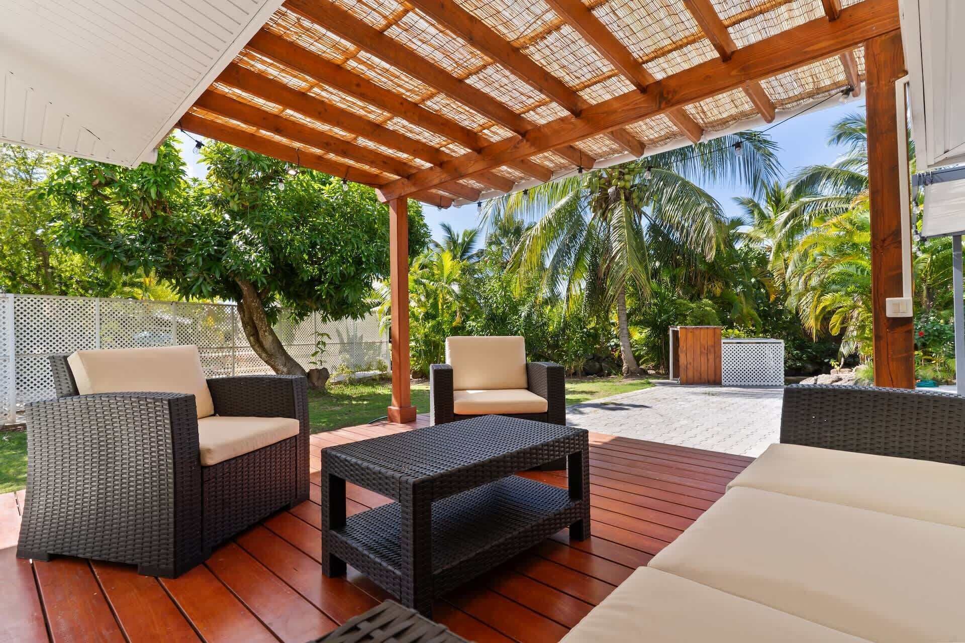 Un patio al aire libre con mobiliario de mimbre, una pérgola y vistas a palmeras.