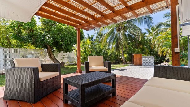 Un patio al aire libre con mobiliario de mimbre, una pérgola y vistas a palmeras.