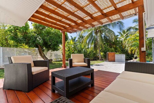 An outdoor patio with wicker furniture, a pergola, and a view of palm trees.