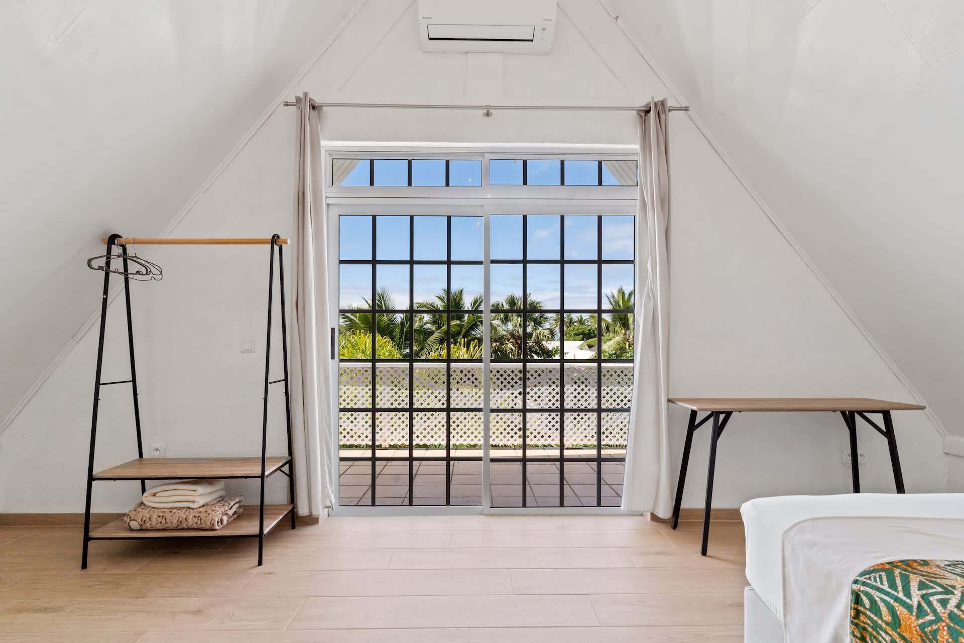 Ein Zimmer mit Bett, kleinem Tisch, Hängekorbschaukel und einem Balkon mit Blick auf Palmen.