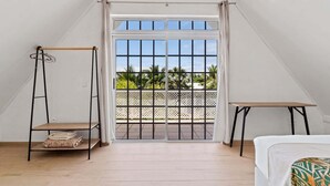 Una stanza con un letto, un tavolino, una sedia a dondolo e un balcone vista palme.
