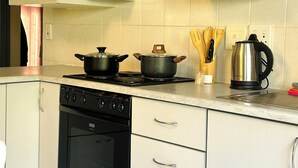 Una cocina con estufa, horno, alacenas y hervidor.