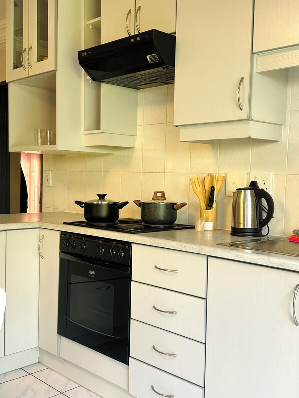A kitchen with a stove, oven, cabinets, and a kettle.
