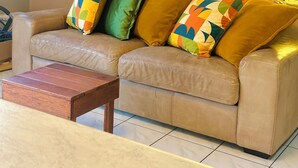 Un sofá de cuero color beige con almohadones coloridos, una mesa de centro de madera y una ventana con cortinas de estampado amarillo.