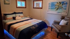 A bedroom with a bed, a chair, a painting, and two windows.