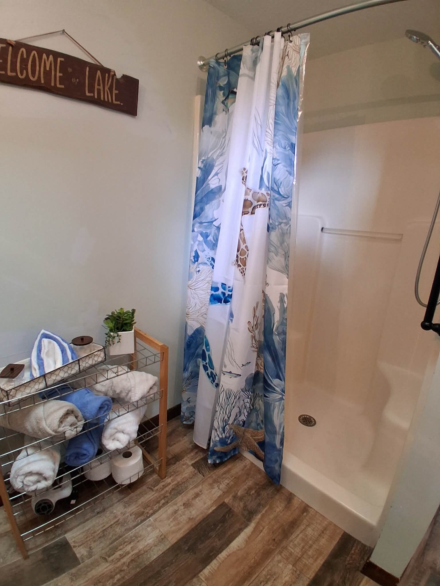 A bathroom with a shower curtain, a towel rack with towels, and a welcome sign.