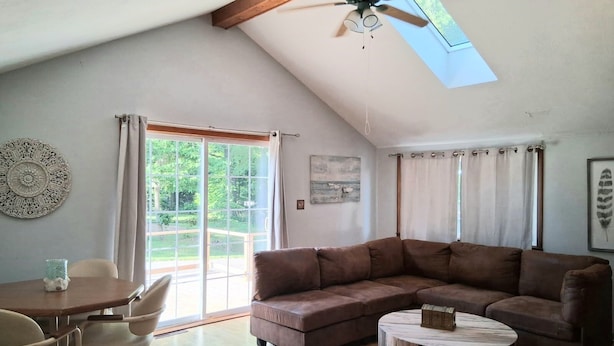A spacious living area with a large brown sectional sofa, a round wooden coffee table, a dining table with chairs, and a ceiling fan.