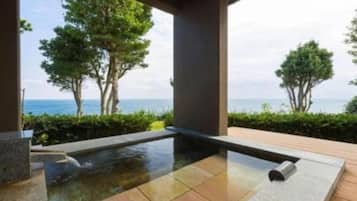 Un espacio de spa con un jacuzzi, terraza de madera y vista al mar.
