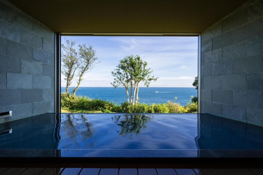 A room with a large glass window, a pool, and a view of the sea.