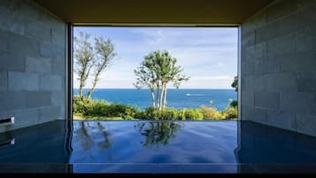 A room with a large glass window, a pool, and a view of the sea.