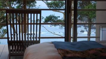 A bed with a view of the ocean through a window with a wooden railing.