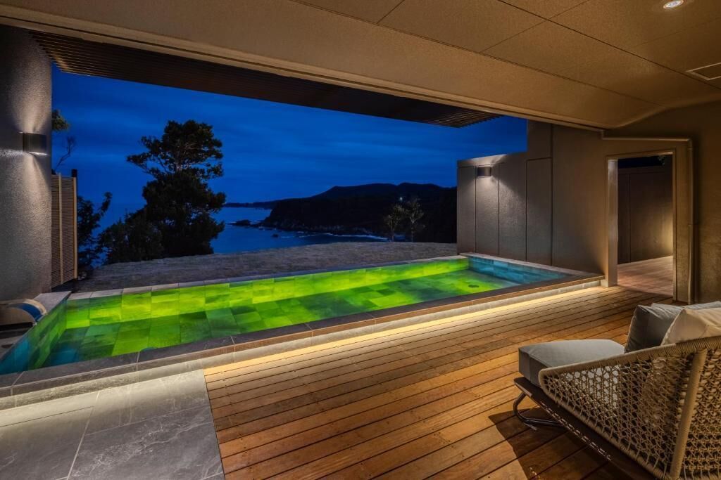 A modern outdoor hot tub area with a view of the sea at dusk.