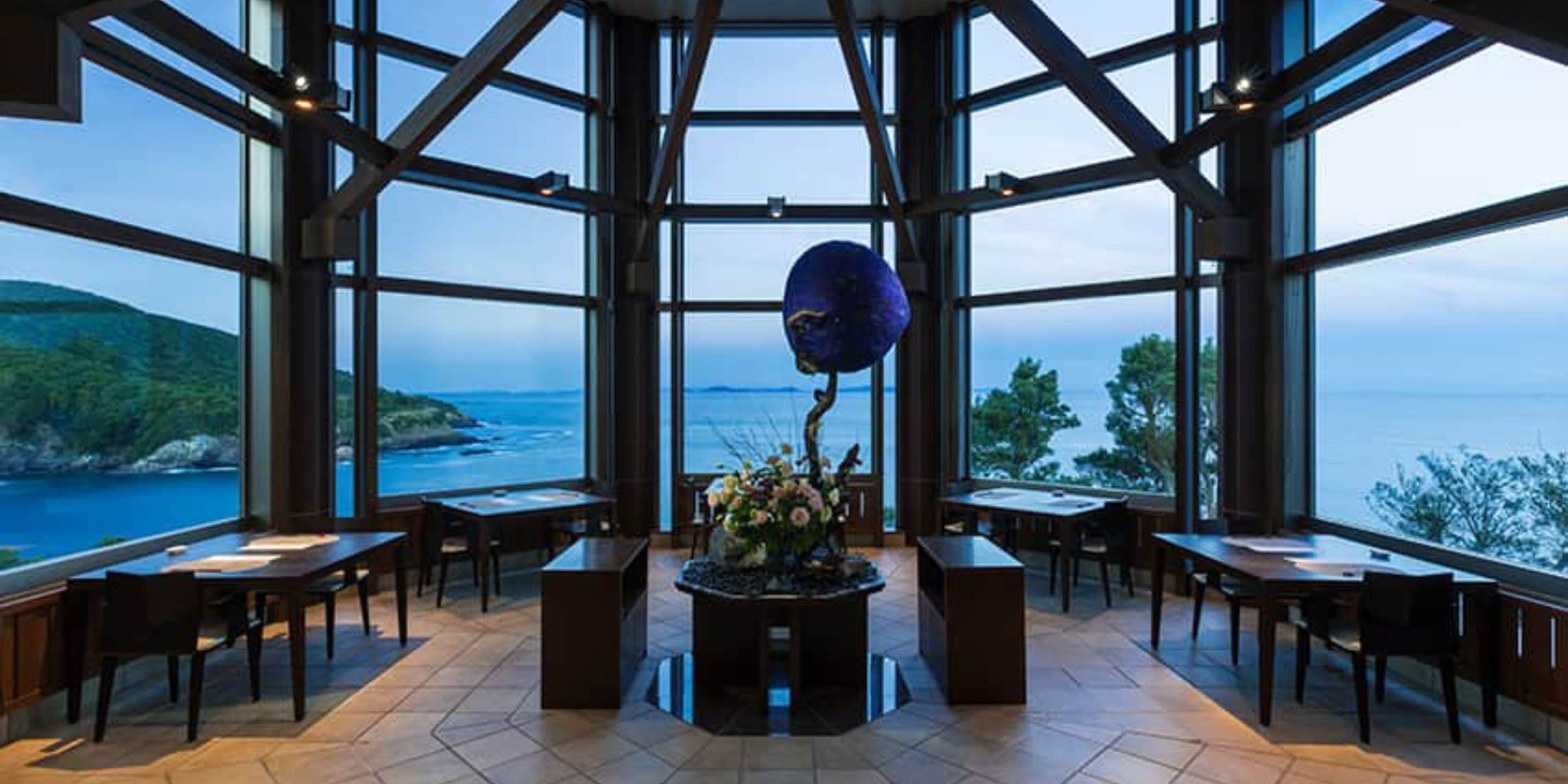 A spacious room with large windows offering a view of the sea and hills.