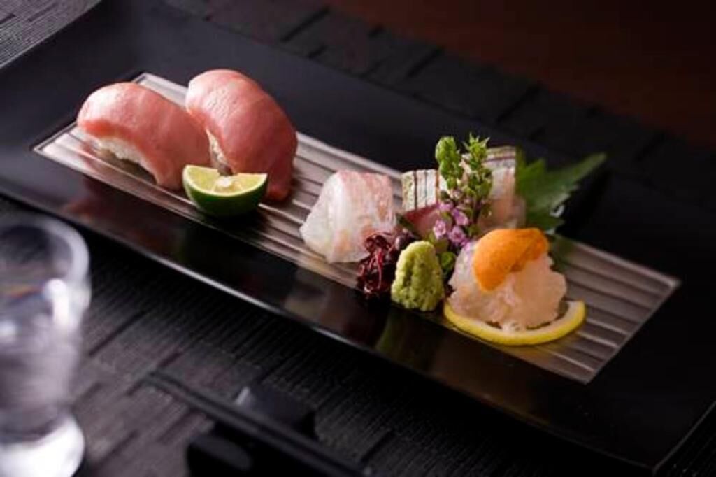 A sushi platter with various types of fish and garnishes on a rectangular plate.