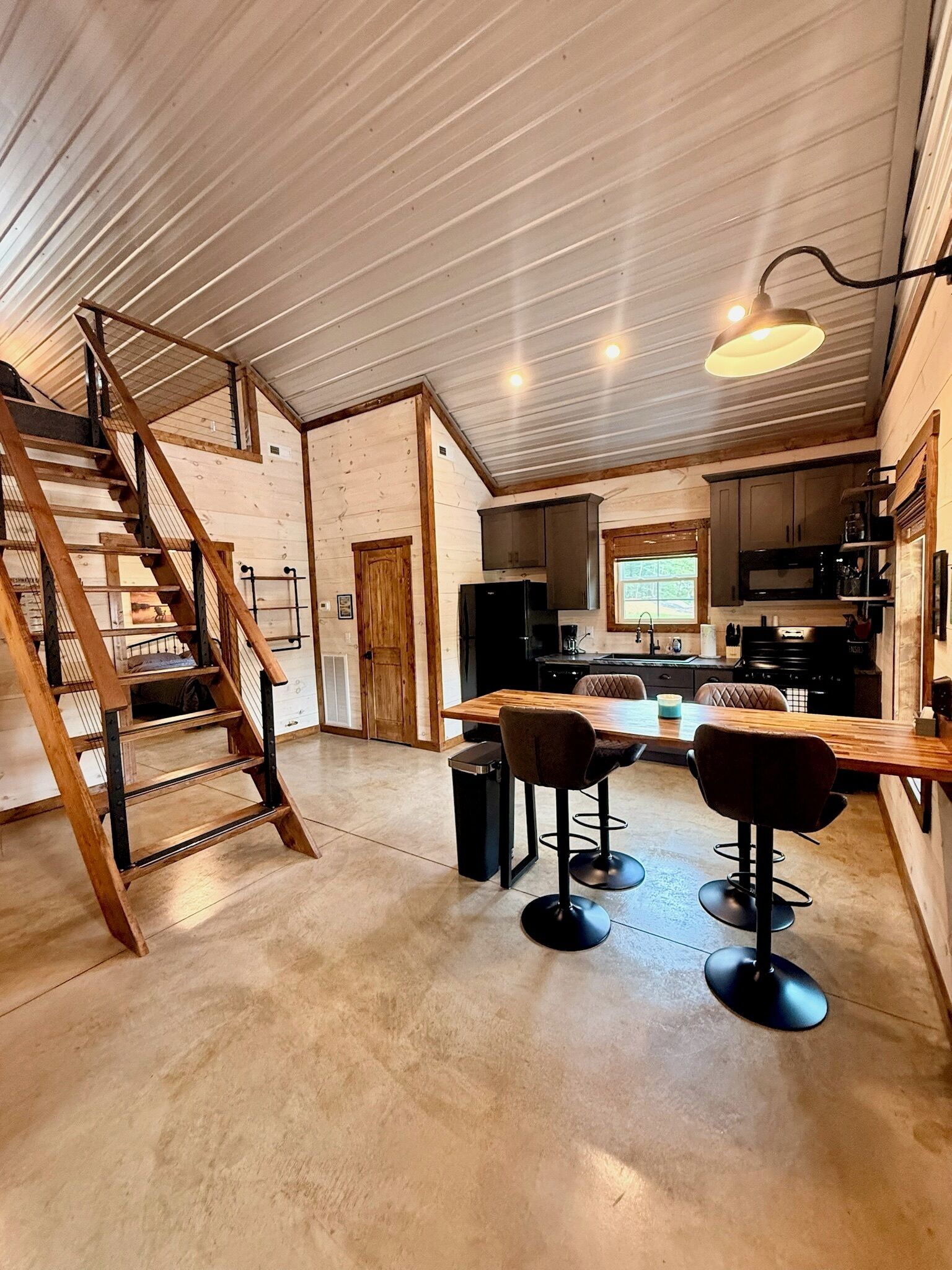 A spacious kitchen with a central island, wooden staircase, and bar stools.