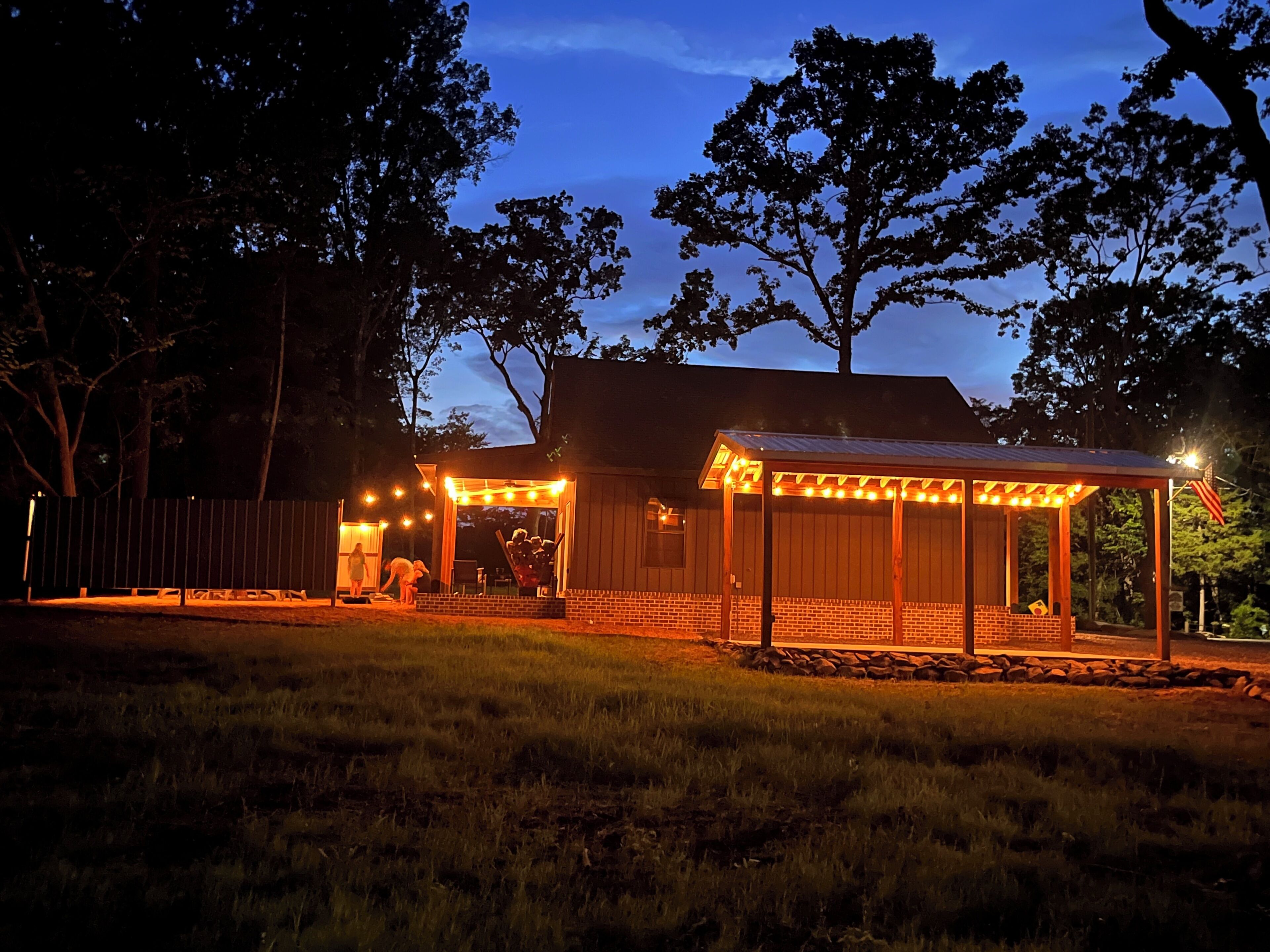 A house with a covered porch, a fenced yard, and trees in the background.