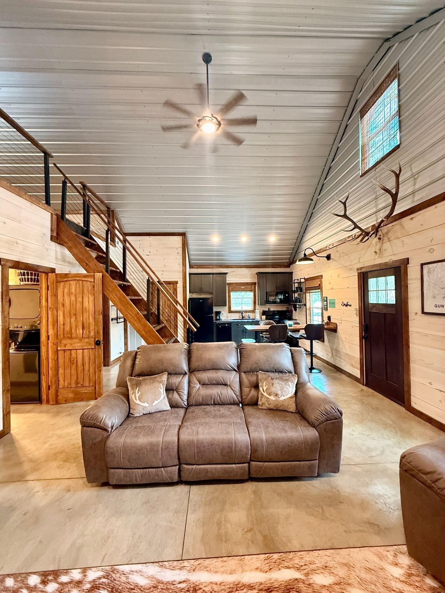 A spacious living area with a large brown leather sofa, a wooden staircase, and a ceiling fan.