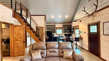 A spacious living area with a large brown leather sofa, a wooden staircase, and a ceiling fan.