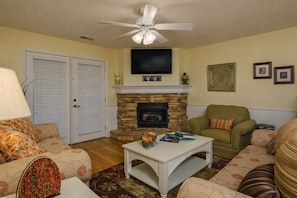 A living room with a fireplace, a ceiling fan, and a television mounted above it.