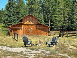 Ein rustikaler Hollboden-Bauernhof mit einer großen Tür und zwei Adirondack-Stühlen davor.