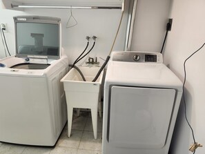 Zona de lavandería con lavadora, secadora y un lavamanos pequeño con mangueras.