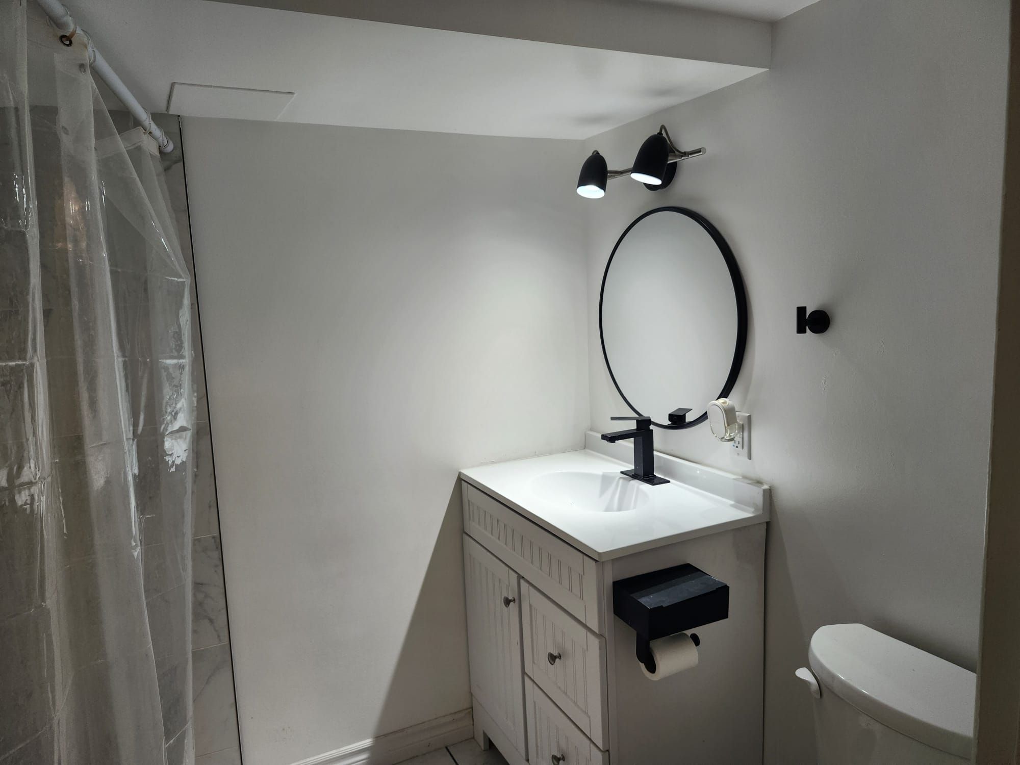 Ein Badezimmer mit einem weißen Waschbecken, einem schwarzen Wasserhahn, einem Spiegel und einer Toilette.