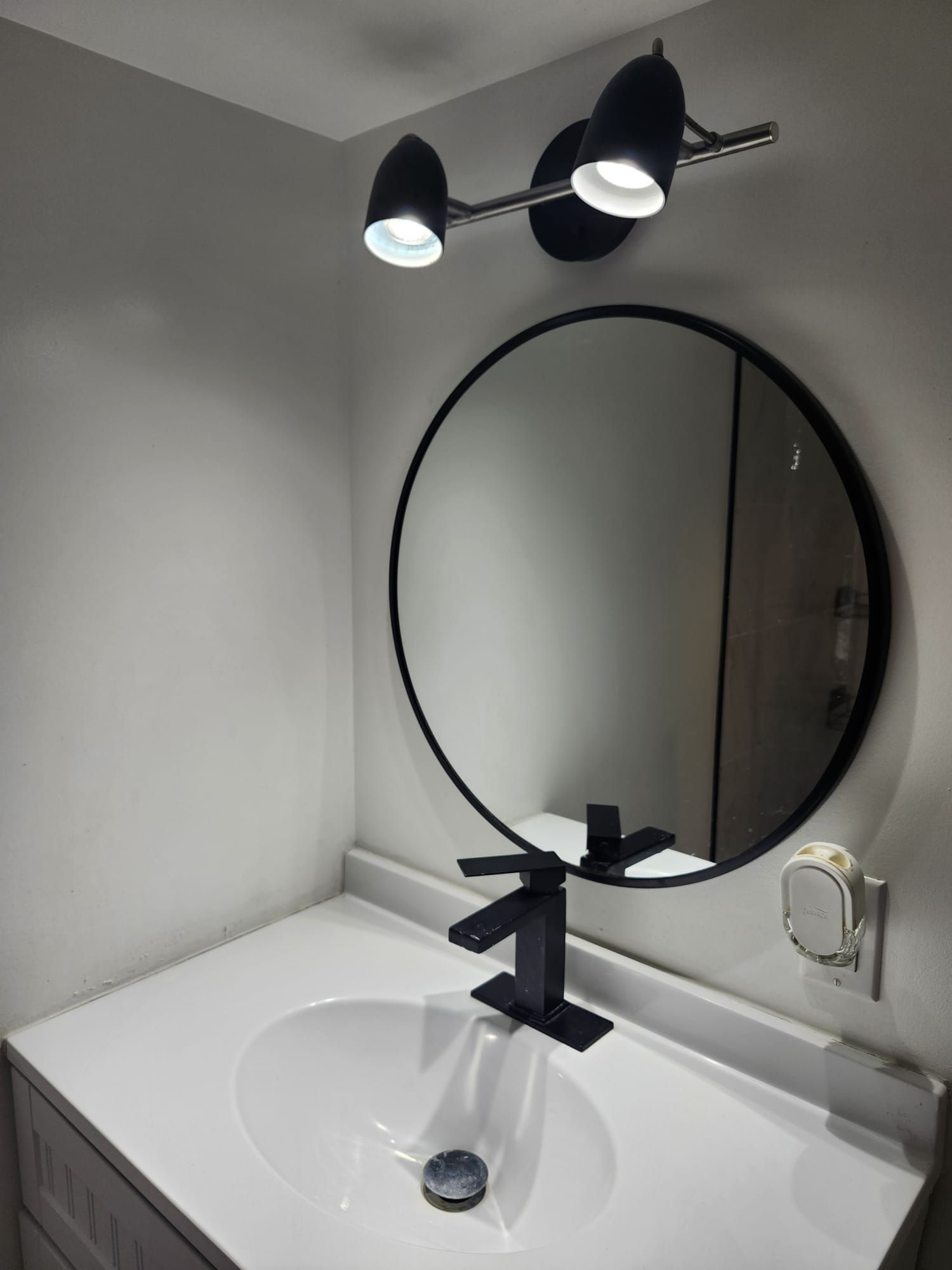 A bathroom with a white sink, a round mirror, and two wall-mounted lights.