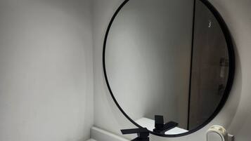 A bathroom with a white sink, a round mirror, and two wall-mounted lights.
