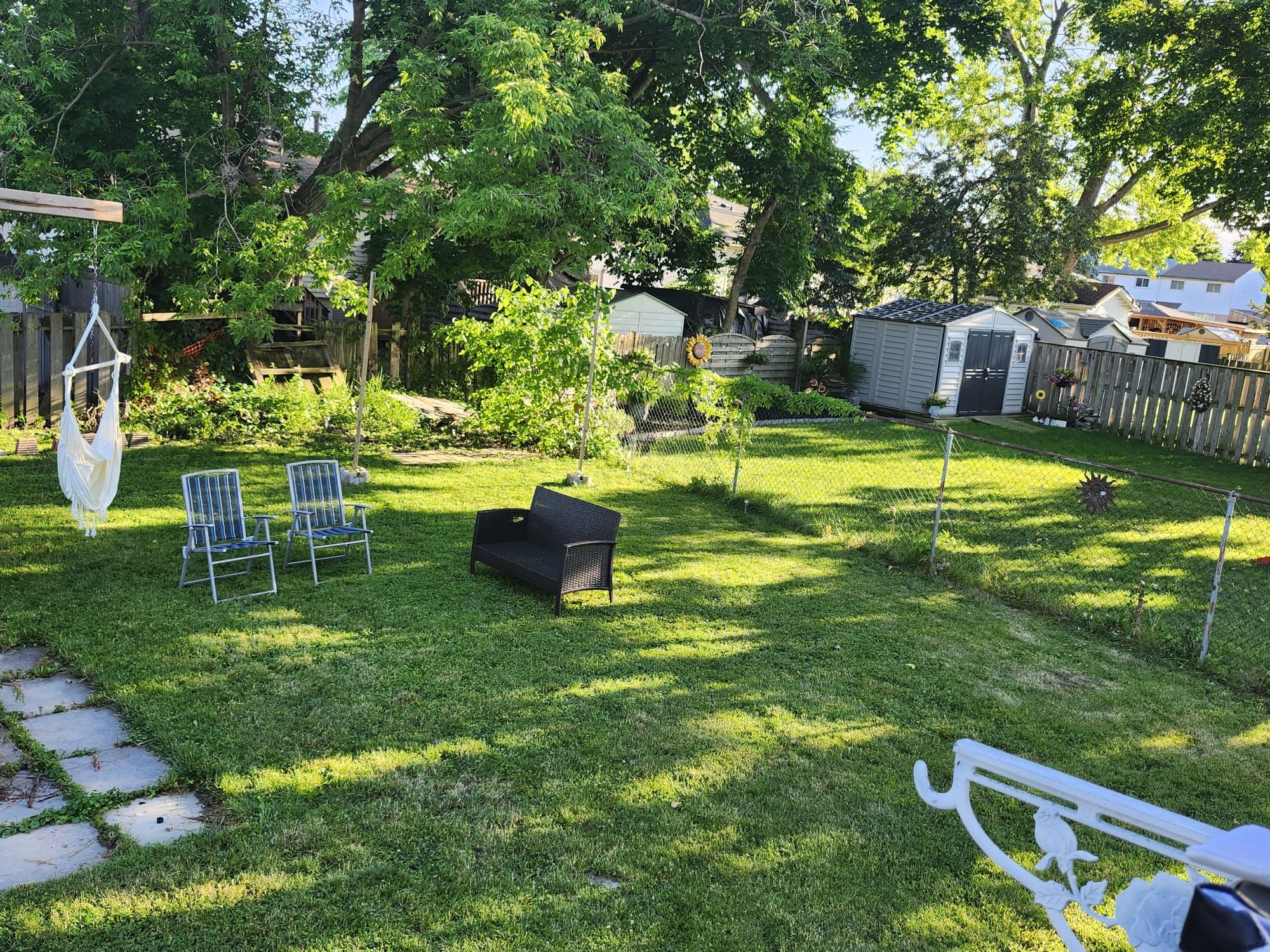 A backyard with a hammock, two chairs, a bench, and a small garden area.