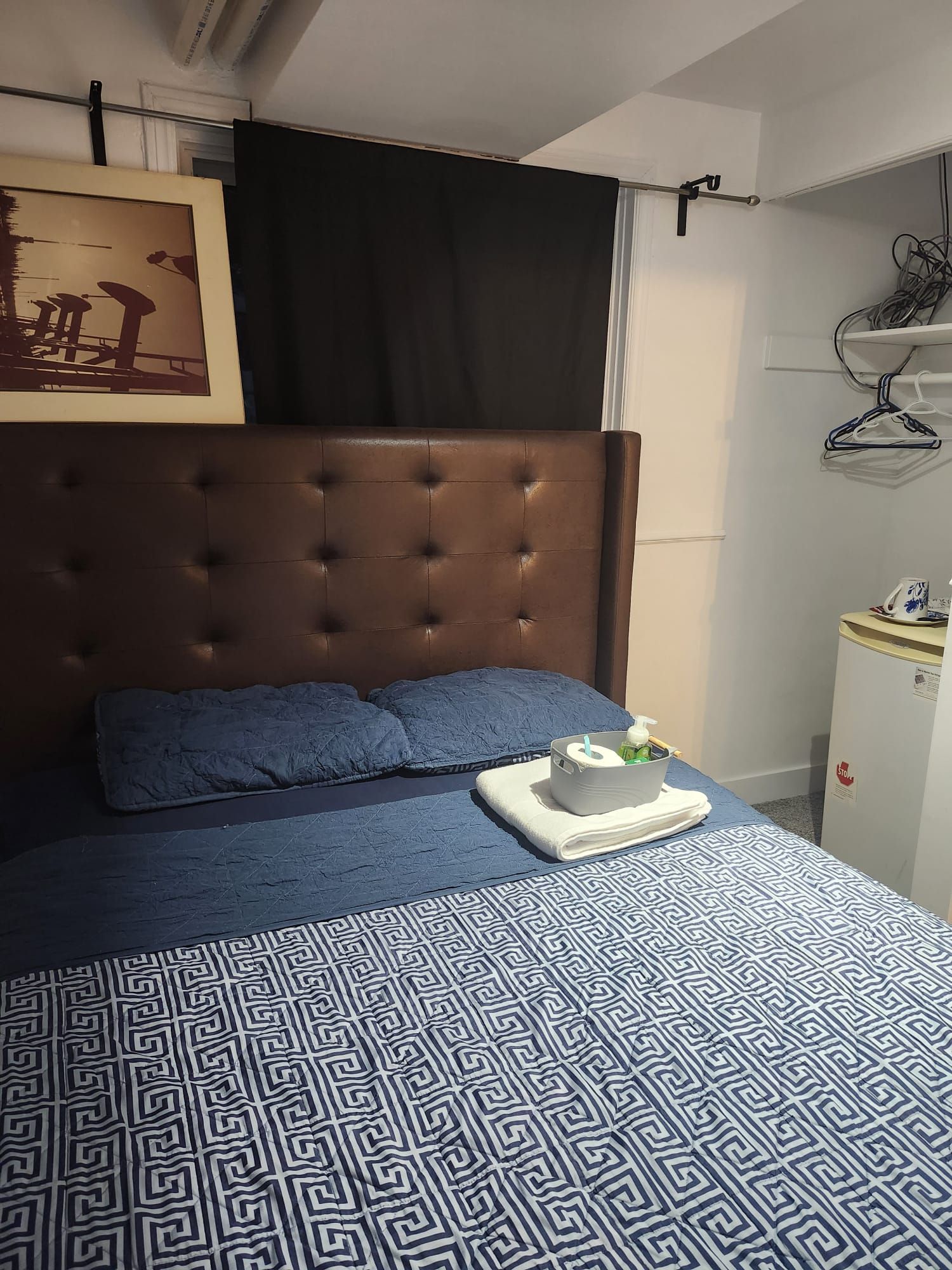 Ein Schlafzimmer mit einer gesteppten Kopfstütze, einer gemusterten Bettdecke und einem Nachttisch mit einem Laptop und einer Tasse.