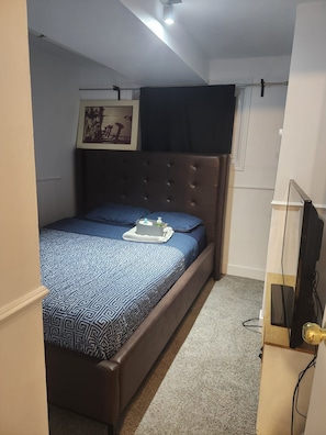 Un dormitorio pequeño y ordenado con una cama, un cuadro en la pared y un televisor sobre un mueble.
