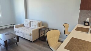 Un salon moderne comprenant un canapé, deux fauteuils, une petite table et un coin cuisine avec un plan de travail et un code QR imprimé sur une carte.