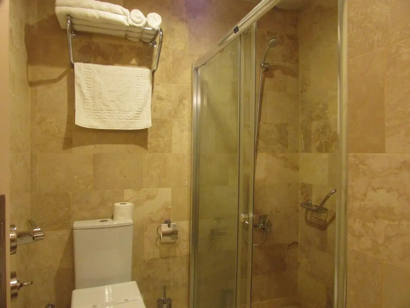 Un baño con ducha de vidrio, inodoro y toallero con toallas.