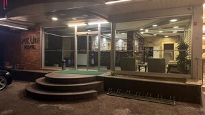 Entrada de um hotel com fachada de vidro, uma escadaria e um carro estacionado em frente.