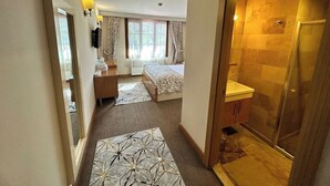 Quarto de hotel com cama, secretária, chuveiro e vista para o exterior.