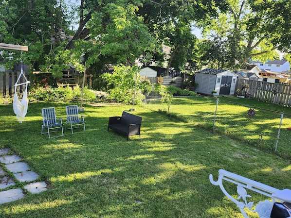 A backyard with a hammock, two chairs, a bench, and a small garden area.