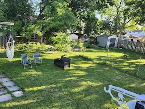 Un patio trasero con una hamaca, dos sillas, un banco y un pequeño jardín.