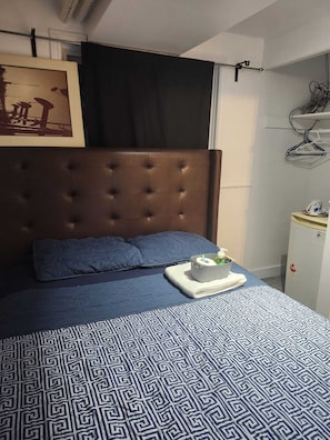 A bedroom with a tufted headboard, a patterned bedspread, and a bedside table with a laptop and a cup.