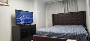 A bedroom with a television on a cabinet, a bed with a patterned bedspread, and a window with curtains.